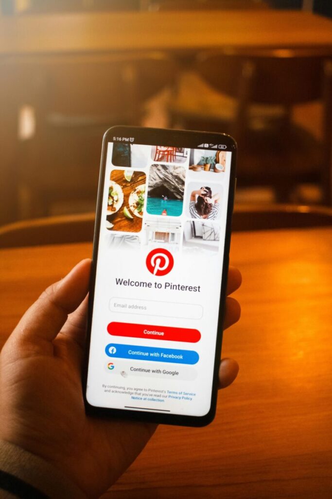 Close-up of a hand holding a smartphone displaying the Pinterest login screen indoors.